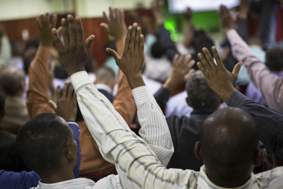 Medlemmene i Assemblies of God Ministry i Coreia-favelaen i Rio de Janeiro, løfter hendene under et møte med pastor Dione dos Santos. De fattige og ofte mørkhudede i favelaene identifiserer seg med pinsepastorene som gjerne har samme bakgrunn. De katolske prestene er ofte hvite, har høyere utdanning og sees derfor på som en del av eliten. Foto: Felipe Dana/AP photo/NTB scanpix
