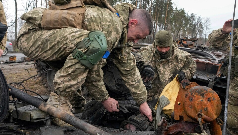 ETTER SLAGET: Ukrainske soldater løfter ut en død russer fra en stridsvogn etter slaget Dmytrivka. En video avslører angivelig ukrainske soldater som henretter sårede, russiske soldater. Ukrainian soldiers try to pull a dead body of a Russian soldier from the destroyed Russian tank in the village of Dmytrivka close to Kyiv, Ukraine, Saturday, Apr. 2, 2022. At least ten Russian tanks were destroyed in the fighting two days ago in Dmytrivka. (AP Photo/Efrem Lukatsky)