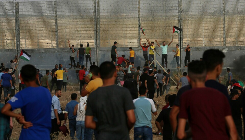 DEMONSTRERER: Demonstranter forsøker å klatre over grensegjerdet mellom Gazastripen og Israel under en demonstrasjon lørdag 21. august. Demonstranter forsøker å klatre opp på gjerdet som skiller Gazastripen fra Israel, under lørdagens demonstrasjon. Foto: Adel Hana / AP / NTB