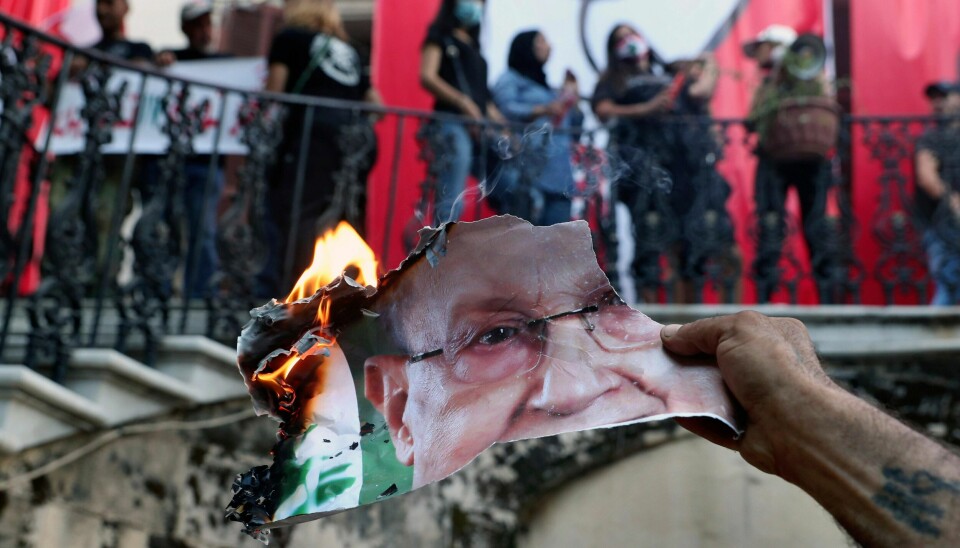 I dette bildet fra 8. august, brenner en demonstrant et bilde av den libanesiske presidenten Michel Aoun inne utenriksdepartementet i Beirut, Libanon. Til tross for press om å gå av, sier presidenten nå at et slikt scenario vil være «umulig». (AP Photo/Bilal Hussein, File)