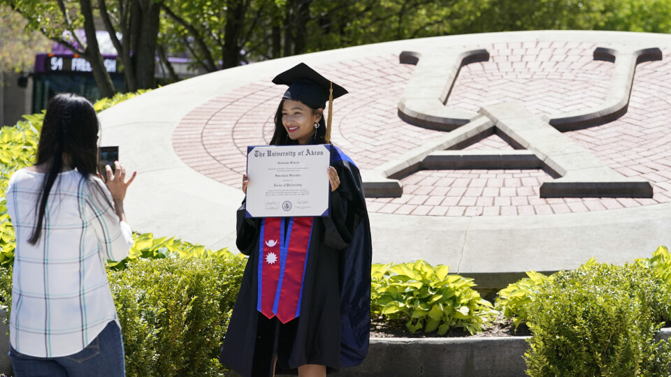 STIPEND: Studenten Sulochana Shrestha poserer for søsteren Sushma 13. mai i Ohiho. Hun er ferdig med college, men fem andre studenter kan vinne fire års stipend. Det er et ledd i å få flere til å vaksinere seg i Ohio. Recent University of Akron graduate Sulochana Shrestha, right, poses for a photo taken by her sister, Sushma, on campus, Thursday, May 13, 2021, in Akron, Ohio. Ohio Gov. Mike DeWine recently announced a weekly $1 million prize and full-ride college scholarships to entice more Ohioans to get the COVID-19 vaccine. (AP Photo/Tony Dejak)