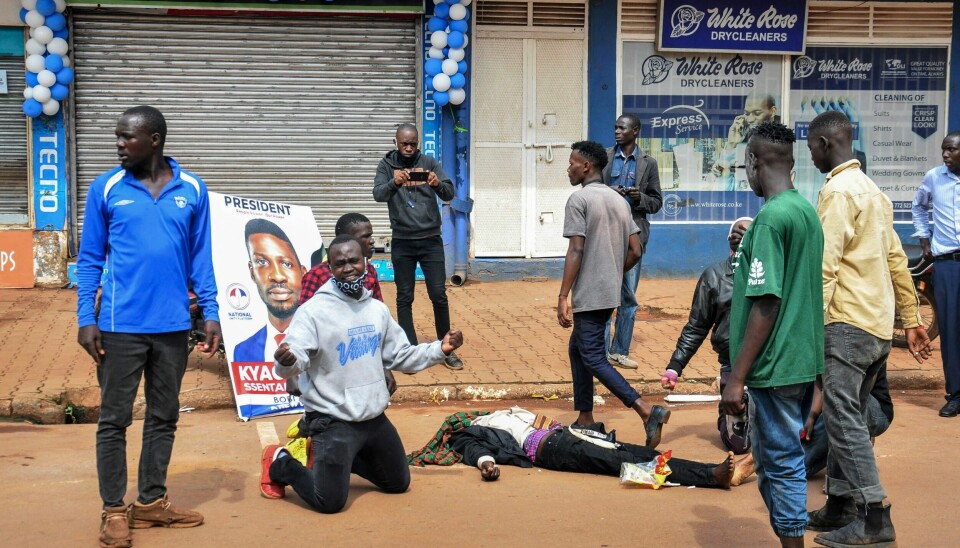 54 mennesker ble drept i Uganda under protester 17. og 18. november i fjor. Her fortviler tilhengere av opposisjonskandidat Bobi Wine (avbildet på plakaten) ved siden av en demonstrant de hevder er drept av politiet. Torsdag går det nytt gjenvalg for president Yoweri Museveni, etter en valgkamp preget av vold og kaos.