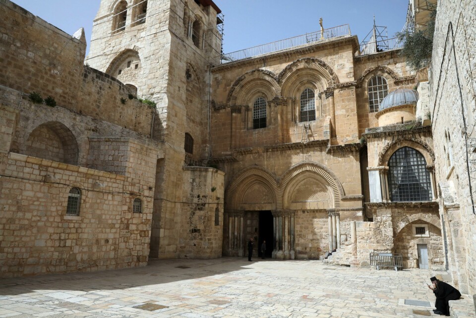 En prest sjekker telefonen utenfor Gravkirken i Jerusalem. An Orthodox Christian priest checks his phone at an empty plaza in front to the Church of the Holy Sepluchre, where Christians believe Jesus Christ was buried, in Jerusalem, Monday, March 23, 2020. In Israel daily life has largely shut down with coronavirus cases multiplying greatly over the past week, (AP Photo/Mahmoud Illean)