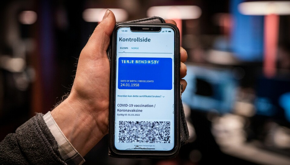 KORONAPASS: Slik ser koronapasset for EØS/EU ut. Ordningen bør fjernes, mener Folkehelseinstituttet. Bildet er av en hånd som holder opp en mobil. Skjermen viser et blått koronapass. Foto: Ole Berg-Rusten / NTB