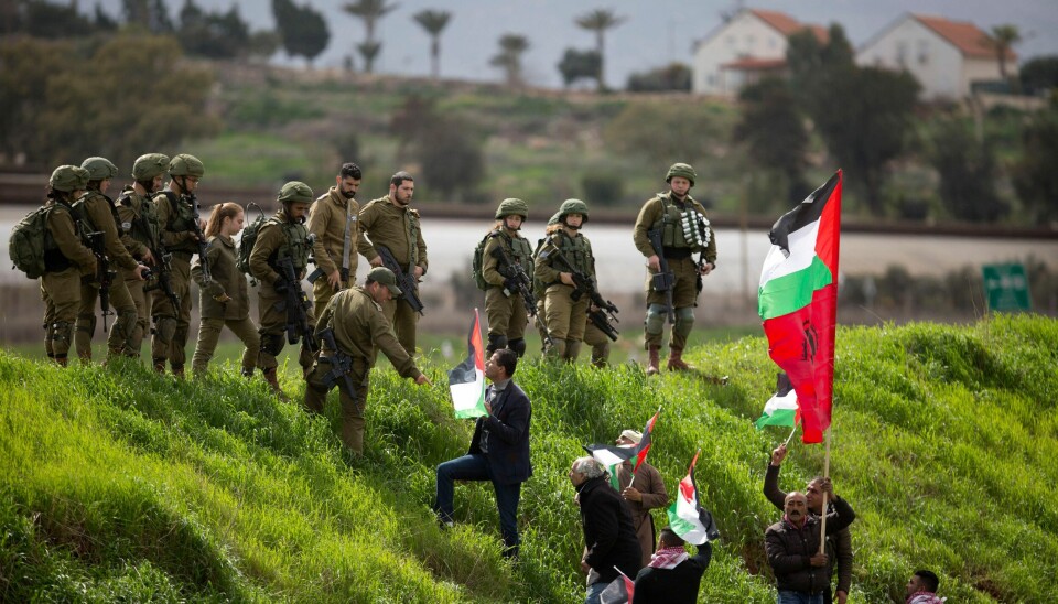 Palestinian demonstrators hold a national flag in front of Israeli forces as they protest against U.S. President Donald Trump's Mideast initiative, near a Jewish settlement Beqa'ot in Jordan Valley in the West Bank, Saturday, Feb. 29, 2020. (AP Photo/Majdi Mohammed).