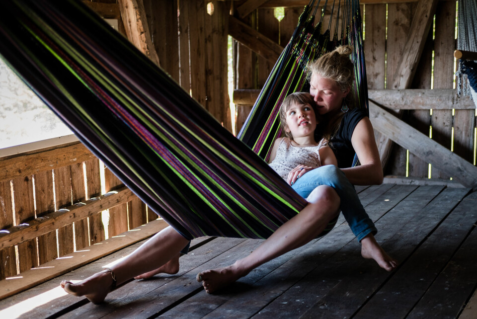 Frida (5) slapper av på mamma Julia Skaara Wiks fang i en hengekøye på hemsen på den gamle låven på gården. Snart skal bygget gjøres om til scene under den årlige sommerfesten.