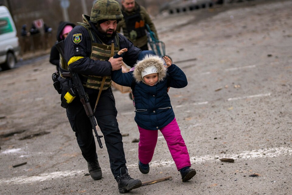 TRYGGLEIK: Ein politimann hjelper eit barn over gata og i tryggleik under eit russisk åtak på Kyiv. En barn blir hjulpet i sikkerhet av en politimann under et russisk angrep mot utkanten av Kyiv tidligere i måneden. Foto: AP / NTB