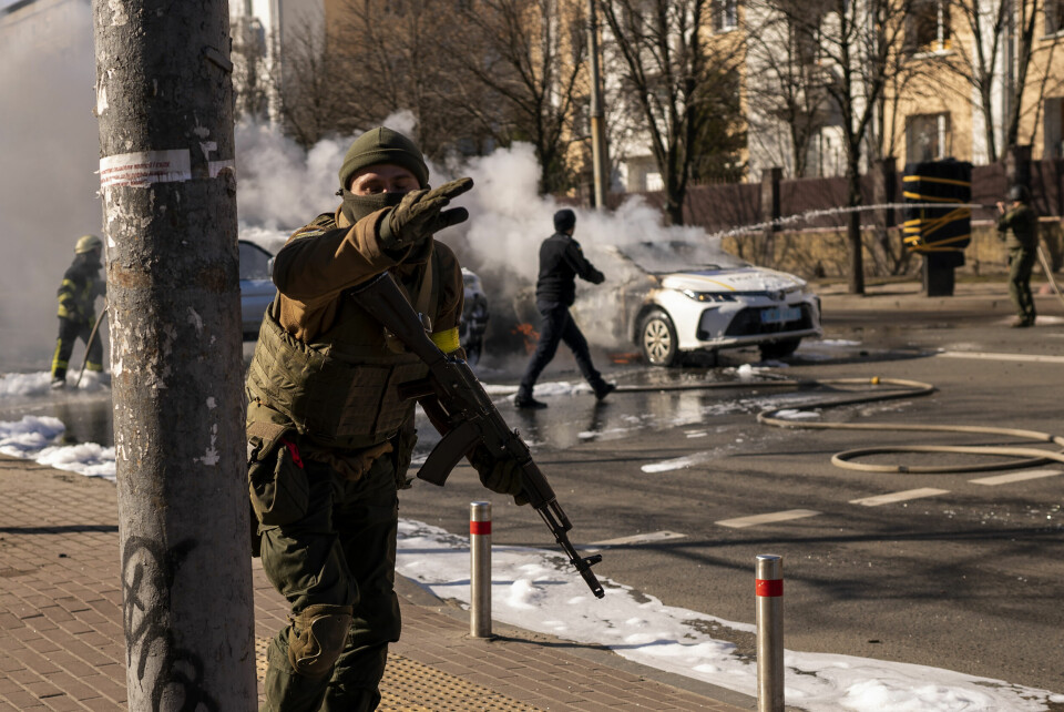 I STILLING: Ukrainske soldater tar stilling utenfor et militæranlegg mens to biler står i brann i Kyiv lørdag. Ukrainske soldater tar stilling utenfor et militæranlegg mens to biler står i brann i Kyiv lørdag. Foto: Emilio Morenatti / AP / NTB