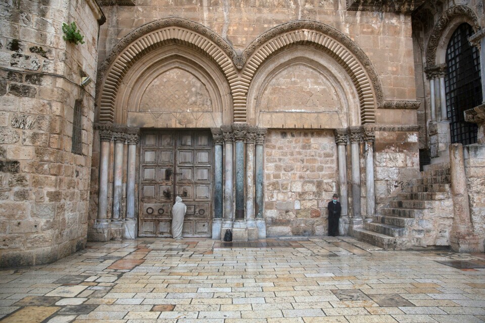 En enslig troende ber foran den stengte døren til Den hellige gravs kirke i Jerusalem langfredag. En sikkerhetsvakt passer på. Kirken, som er svært sentral i den kristne påskefeiringen, er stengt på grunn av koronapandemien. A Christian stands at the closed door of the Church of the Holy Sepulchre, believed by many Christians to be the site of the crucifixion and burial of Jesus Christ, in Jerusalem, Friday, April 10, 2020. Christians are commemorating Jesus' crucifixion without the solemn church services or emotional processions of past years, marking Good Friday in a world locked down by the coronavirus pandemic. (AP Photo/Sebastian Scheiner)