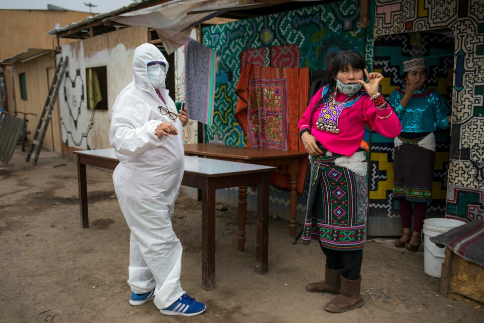 88 prosent av intensivenhetene i Peru er fulle, og viruset sprer seg fortsatt. Foto: Rodrigo Abd/AP. Olinda Silvano from the Shipibo Conibo ethnic group, talks to a member of an NGO dressed in protective gear against the new coronavirus, during the celebration of the feast of Saint John the Baptist, the patron saint of the Peruvian Amazon, in the Cantagallo neighborhood of Lima, Peru, Wednesday, June 24, 2020. The neighborhood reopened about 10 days ago after it had been under strict quarantine due to an outbreak of COVID-19. (AP Photo/Rodrigo Abd)