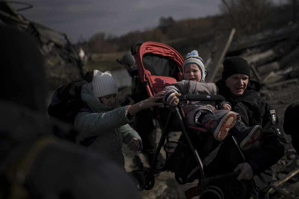 FLUKT: Eit barn i ei barnevogn blir løfta fram av folk på flukt frå byen Irpin i Ukraina. barn